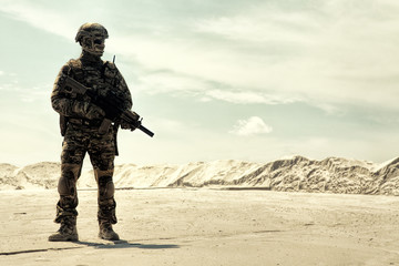 Special operations forces soldier in camouflage combat uniform, helmet and glasses walking in desert with service rifle in hands low angle view. War conflict, military campaign in Middle East region - Powered by Adobe