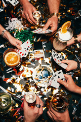 cropped image of friends with alcoholic cocktails playing poker at table covered by golden confetti