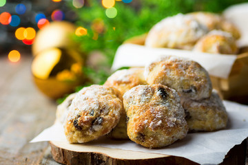 Traditional German Christmas pastry mini stollen on parchment paper on plank wood table. Fresh green juniper branch golden balls colorful garland lights. Rustic vintage style. Festive atmosphere