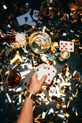 cropped image of man with playing cards and alcohol sitting at table covered by golden confetti