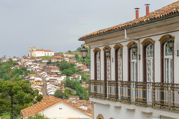 Casarão colonial no centro da cidade histórica brasileira de Ouro Preto com Igreja de Santa Ifigênia e casario em ladeira abaixo ao fundo.