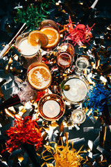 top view of various alcoholic cocktails and party horns on table covered by golden confetti