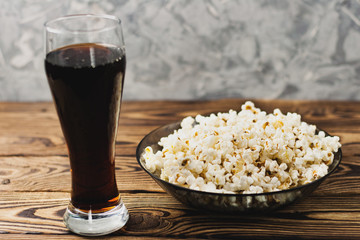 Full glass plate of fried popcorn and glass of sparkling water on wooden table on background of cement wall. The concept of leisure