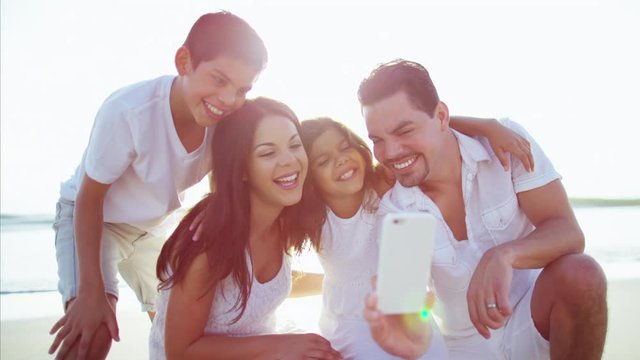 Young Latin American family using mobile technology on the beach