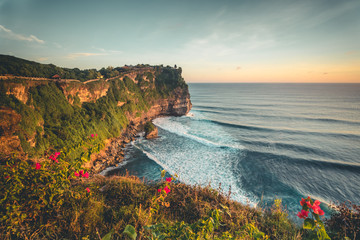 Overview panorama ocean shore, cliff. Sunset. Bali. Overwhelmed scene the flower and green-capped vertical cliff over the Indian ocean. South of Bali island, Pura Luhur Uluwatu Temple. Indonesia.
