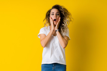 Beautiful young blonde woman jumping happy and surprised over isolated yellow background