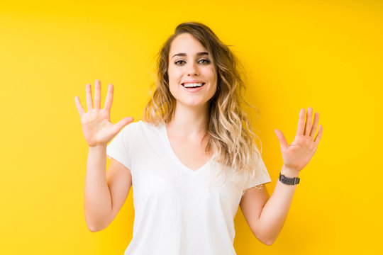 Young beautiful blonde woman over yellow background showing and pointing up with fingers number ten while smiling confident and happy.