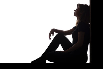 silhouette of a woman sitting on the floor in a corner on a white isolated background, a sad girl...