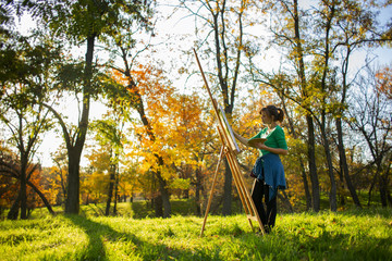 woman drawing a picture on canvas on an easel in nature, a girl with a brush and a palette of paints in beautiful landscape, a concept of hobby