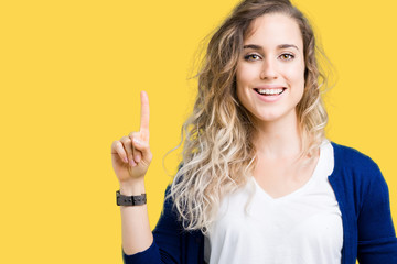 Beautiful young blonde woman over isolated background showing and pointing up with finger number one while smiling confident and happy.