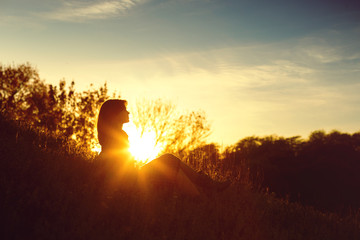 silhouette of a young woman sitting on a hill at sunset in autumn, the concept of human and nature