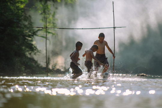 Asian children play soccer in the river,Sport plays an important role in rural and regional Thailand,Sport are the predominantly or exclusively played in rural areas,.