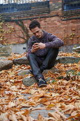 Fototapeta premium Young handsome man sitting on a rock in meadow with foliage and speaking with smartphone