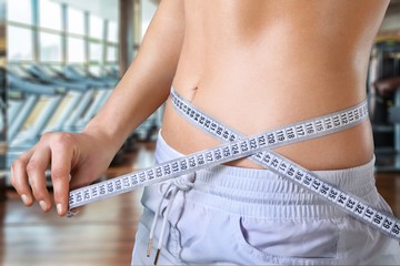 Slim young woman measuring her thin waist with a tape measure
