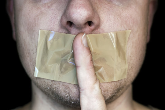 Zugeklebter Mund mit Zeigefinger als Zeichen einer Verschw&ouml;rung
