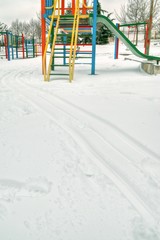 Snow on the colorful children playground in the park. Tracks on the white ground. Winter play and activity concept.