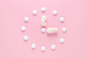 concept image, a clock with candy and marshmallow in pastel colors on pink