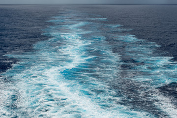 Foam trail in the sea behind the stern of the ship against the horizon