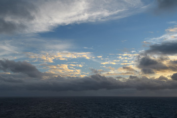 Dark sunset sky over the ocean. Illuminated by the setting sun clouds on the background of blue gaps.