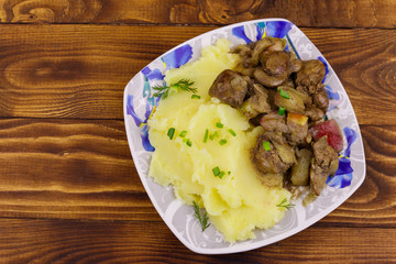 Mashed potatoes with stewed chicken liver with apple and onion on wooden table