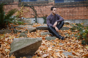 Fototapeta premium Young handsome man sitting on a rock in meadow with foliage