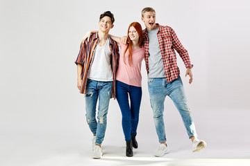 Two guys and a girl in stylish bright colorful clothes walk and smile on the white background in...