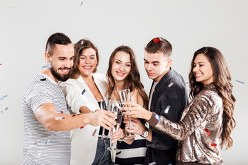 Company of friends in stylish casual clothes stand together and clink glasses with champagne on a white background and confiture around. Party time
