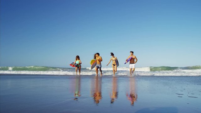 Multi ethnic friends in swimwear jogging with bodyboards on the beach