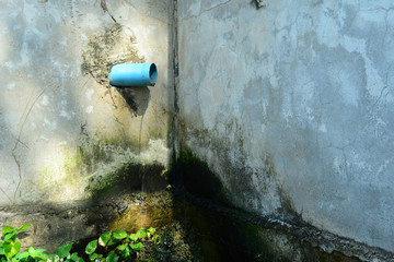 the Water flows out of the blue Sewage pipe at the corner of old cement wall and green plants
