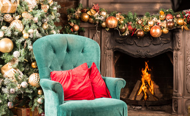 Christmas room, firewood burning in the fireplace, a green armchair with red pillows and a Christmas tree with gifts