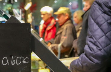 Waiting line at a bakery behind a price board with deliberately blurred people.