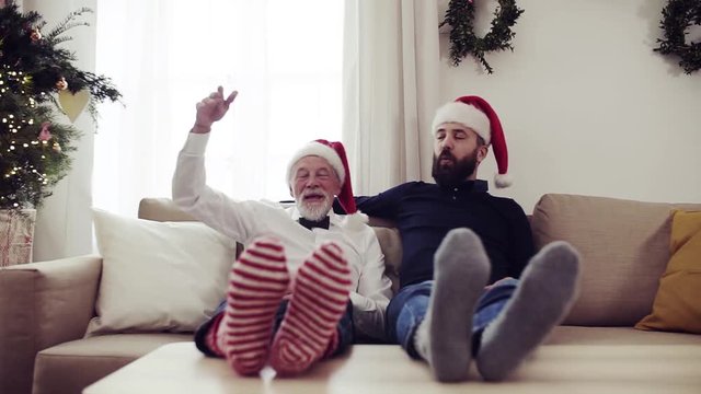 Senior father and adult son sitting on a sofa at Christmas time, having fun.