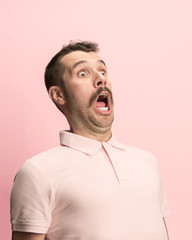 The surprised and astonished young man screaming with open mouth isolated on pink background....