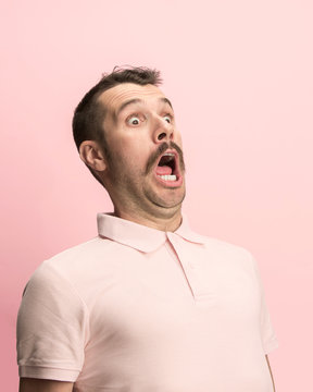 The surprised and astonished young man screaming with open mouth isolated on pink background. concept of shock face emotion