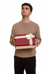 Young handsome Persian man holding gift box while thinking ready