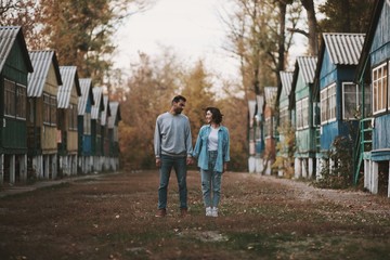 Fototapeta na wymiar Smiling couple stanting with holding hands between row of wooden cabin and looking to each other