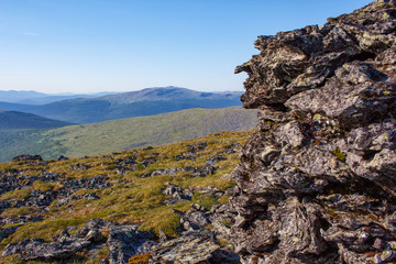 Fototapeta na wymiar Stone peaks on a mountain plateau against a blue sky. The stone wall in the foreground and a beautiful panoramic view of the mountains and the sky. Nature of the Northern Urals.