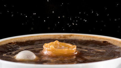 Coffee with cream, splash from a drop of milk on the surface of coffee on a black background