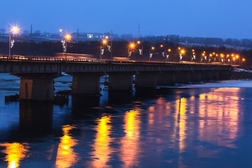 Fototapeta na wymiar Large concrete bridge over the river, illuminated by street lamps.