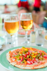 Pizza with mozzarella cheese, olive, fresh tomato and pesto sauce. Served at restaurant table with two beers