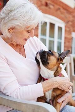 Senior Woman Sitting On Bench With Pet French Bulldog In Assisted Living Facility