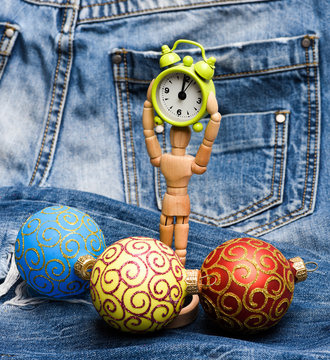 Wooden human body toy hold clock near christmas decoration ball. Christmas decorative toys. Wooden model and ornaments. Christmas decorations concept. Christmas decorations denim background close up
