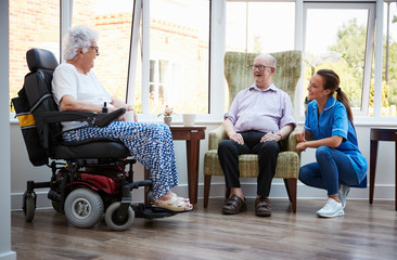 Male And Female Residents Sitting In Chair And Talking With Nurse In Retirement Home - obrazy, fototapety, plakaty