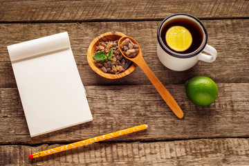 Empty notepad and pencil on the wooden table. Cup of tea, lime and sugar on rustic background.