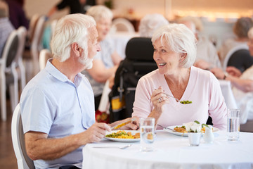 Senior Couple Eating Meal And Talking In Retirement Home - obrazy, fototapety, plakaty