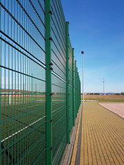 Fototapeta premium A green metal mesh wedge separates the two spaces used. Protection of the territory from outsiders. Modern construction and arrangement of the adjacent territory. Green grass field and modern pavilion