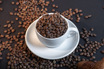 Close up of coffee cup and croissant in coffee beans on black background.