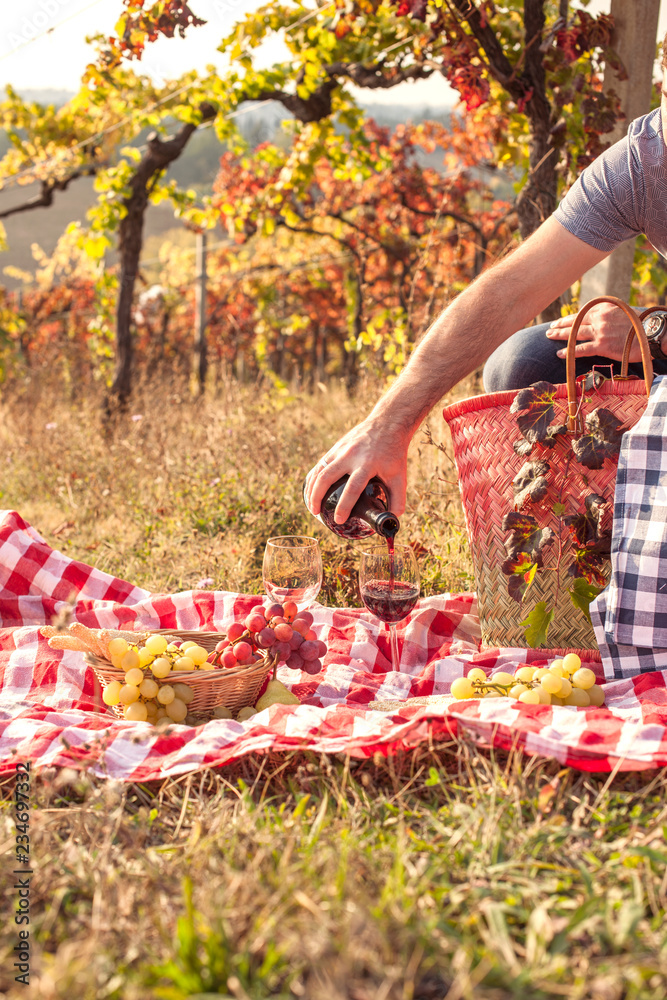 Wall mural Picnic at sunset in the hills of Italy. Vineyards and open nature in the fall. Romantic dinner, a man pours a glass of red wine. Free space for text. Copy space.