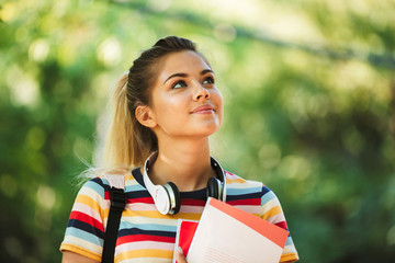 Happy young cute girl student walking in park with backpack.