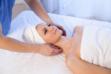 a massage therapist makes a beautiful woman face and body medical massage in the Spa